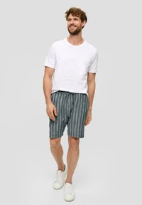 Weißes kurzärmliges Hemd kombiniert mit navyblauen gestreiften Shorts mit elastischem Bund. Getragen mit weißen Sneakers. Neutraler Hintergrund.