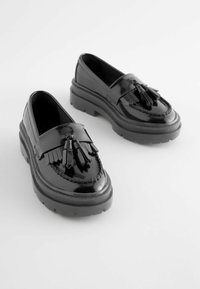 Sorte patentlæder loafers med frynsede detaljer, chunky såler, vævet dekoration langs de øverste kanter og en glat, skinnende tekstur.