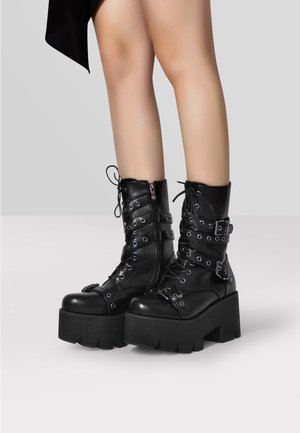 Czarne botki na platformie z syntetycznej skóry, z sznurowaniem, srebrnymi oczkami, regulowanymi paskami, zapięciem na zamek błyskawiczny oraz chunkowymi, fakturowanymi podeszwami.