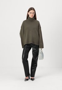Overdimensjonert olivengrønn strikket genser med ribbestrikket høyhalset krage, kombinert med svarte faux skinnbukser og en lys blå veske.