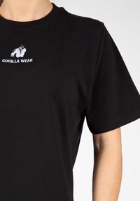 Zwarte katoenen t-shirt met een ronde halslijn en korte mouwen. Centraal wit geborduurd logo met de tekst "GORILLA WEAR" erboven.