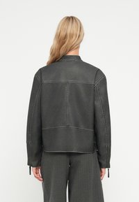 Giacca in finta pelle grigia con un design strutturato, cuciture visibili e una vestibilità dritta. Presenta due polsini con zip e un retro pulito.