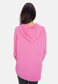 Rosa Pullover-Hoodie aus leichtem, strukturiertem Material, mit Kapuze und Kordelzug, entspannter Passform, langen Ärmeln und abgerundetem Saum.