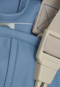 Ljusblå ryggsäcksmaterial med texturerad tyg, med beige rem- och spänndetaljer. Slät yta med snyggt sydda accenter.