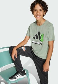 Zelené bavlněné tričko s grafikou Minecraft, černé tepláky s pixelovou postavou a černé tenisky s bílými pruhy.