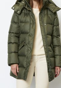 Olijfgroene pufferjas met capuchon, drukknoop- en ritssluitingen, met een doorgestikte textuur en zijzakken.