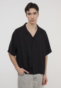 Camicia nera a maniche corte con vestibilità rilassata, colletto a revers e chiusura con bottoni; realizzata in tessuto morbido con una leggera lucentezza.