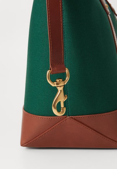 Sac textil verde cu bază din piele maro, având un închizător din metal aurit și detalii de cusătură. Designul evidențiază materiale și culori contrastante.