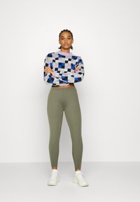 Multi-colored checkered knit sweater with long sleeves, paired with olive green stretchy leggings and white athletic shoes.