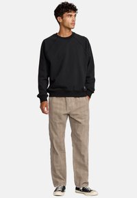 Zwarte sweatshirt met een ronde hals en raglanmouwen, gecombineerd met lichtbruine geruite broek en zwarte sneakers met witte zolen.