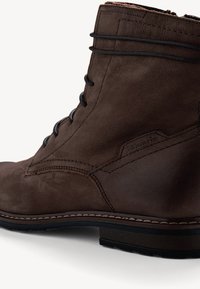 Bottine en daim marron avec des lacets noirs, des coutures détaillées et une semelle en caoutchouc. Présente un logo subtil de la marque sur le côté.
