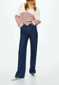 Pull crème à rayures rouges, manches larges, associé à un jean en denim bleu foncé taille haute. Chaussures argentées à bout pointu apportant de l'éclat.