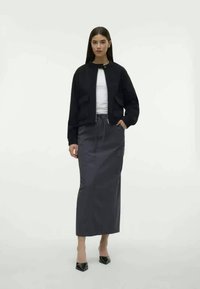 Must must sindel mustan jope valge ülikonna peal, kombinatsiooniks kõrge vöökoht hall seelik. Seelik on pikk ja sujuv, mida täiendab teravotsaga mustad kontsad.