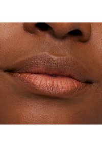 Nærbilde av fyldige lepper med en matt nude leppestift, jevn tekstur, varm brun hudtone og et naturlig leppekontur.