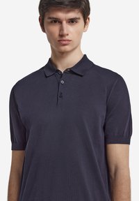 Mörkblå kortärmad polo av klassisk modell, med krage, tre knappar och en slät yta. Enkel design utan synliga mönster.