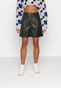 Shorts en cuir noir à texture lisse, avec une coupe ajustée et un ourlet retroussé. Associés à un pull court à carreaux multicolores.