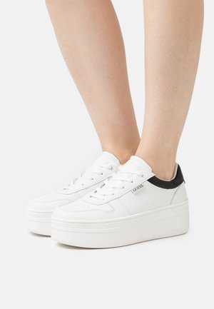 Zapatillas de plataforma blancas con parte superior de cuero liso, acento negro en el talón, puntera perforada y cordones visibles. Presenta una etiqueta de marca en el lado.