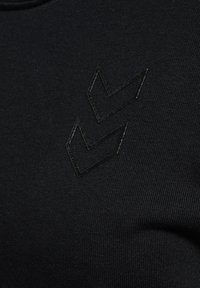 Dwa błyszczące czarne kształty szewronu na czarnej fakturowanej tkaninie, tworzące subtelny, tonalny detal projektowy.