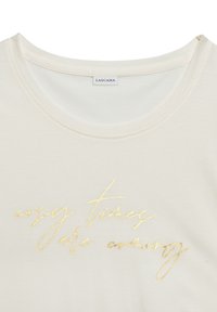 Cream-colored t-shirt with a round neckline and short sleeves; features gold cursive text "cosy times are coming" across the front.