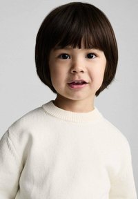 Child wearing a cream-colored, textured knit sweater with a ribbed round neckline, short sleeves, and a friendly expression.