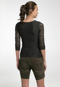 Schwarzes Spitzenhemd mit Dreiviertelärmeln, das mit Blumenmustern und gewellten Kanten verziert ist, kombiniert mit dunkelgrünen Wildleder-Shorts.