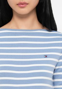 Μακρυμάνικη ριγέ μπλούζα σε ανοιχτό μπλε και λευκό βαμβάκι, με στρογγυλή λαιμόκοψη και μικρή λεπτομέρεια λογότυπου στο αριστερό στήθος.