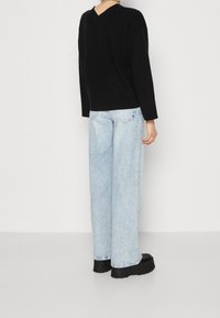 Svart stickad tröja med V-formad rygg, kombinerad med ljusblå vida jeans och svarta platåskor med synliga sömnadsdetaljer.