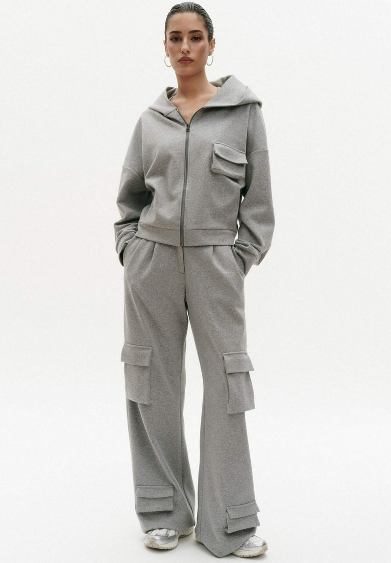 Szary zestaw dresowy z kapturem i spodniami cargo. Hoodie ma zamek błyskawiczny z przodu i jedną kieszeń na piersi. Spodnie mają duże kieszenie boczne i luźny krój.