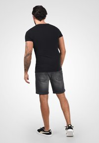 Čierne tričko s krátkym rukávom, slim fit, skombinované s tmavošedými riflovými šortkami s vyhrnutými nohavicami. Čierne tenisky so zlatým akcentom.