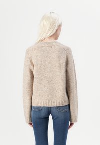 Beige gestrickter Pullover mit Rundhalsausschnitt, langen Ärmeln, geripptem Saum und einer weichen Textur mit subtilen Flecken.