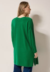 Grön oversized tröja i stickad tyg. Har en djup V-ringning och sidslitsar, med långa ärmar och en avslappnad passform.