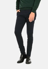 Pantaloni slim-fit blu navy in cotone con una texture liscia, dotati di tasche laterali e un design su misura, abbinati a scarpe in pelle nere.