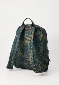 Sac à dos à motif floral en tissu vert foncé et beige, doté de bretelles noires et d'une poignée supérieure, avec une fermeture à glissière et une poche latérale.