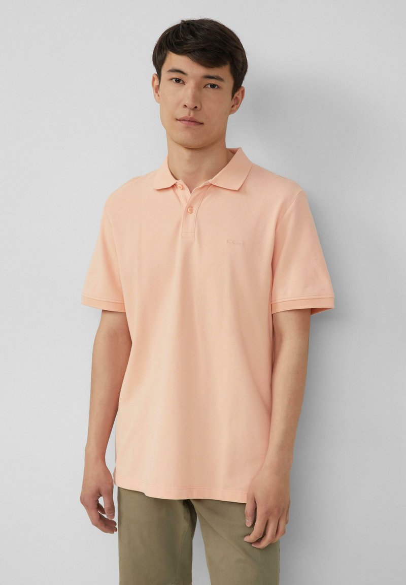 Perzikkleurig poloshirt met korte mouwen, textuurstof, knoopsluiting met twee knopen en geborduurd logo. Gekocht bij kaki broek.