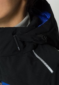 Svart ytterjacka med en snug huva, med blå foder, reflekterande detaljer och justerbar dragsko. Slät textur och funktionell design.