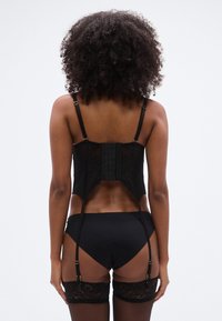 Σετ μαύρου εσωρούχου με μπουστάκι που διαθέτει ρυθμιζόμενες τιράντες, δαντελένιες λεπτομέρειες και κλείσιμο με αγκράφα. Το πίσω μέρος έχει σχεδιασμό με άνοιγμα.