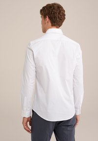 Witte lange mouwen-shirt met een klassieke kraag en knoopmanchetten, met een gladde textuur en een gebogen zoom, gedragen met een grijze broek.