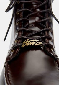 Bruine leren veterschoenen met ronde veters, een messingen logo-label, metalen oogjes en een glanzende afwerking met contrasterende stiksels.