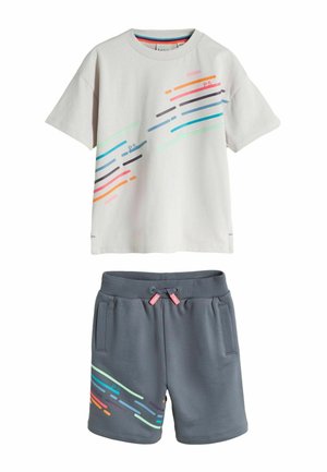 Weißes T-Shirt mit kurzen Ärmeln und bunten diagonalen Streifen, kombiniert mit grauen Shorts mit Kordelzug, die am Bein passende Streifenmuster aufweisen.