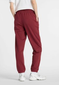 Bordeauxfärgade sweatpants med avslappnad passform, elastisk midja, sidfickor och avsmalnande anklar, tillsammans med vita träningsskor.