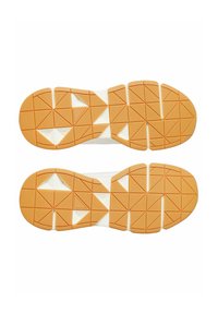 Semelles de chaussures avec un motif géométrique en caoutchouc orange, comportant des grips texturés et des découpes triangulaires, posées sur une base blanche.