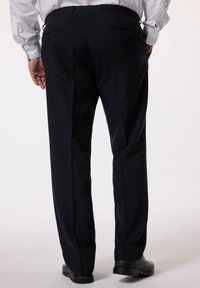 Pantaloni da abito blu navy con vestibilità su misura, davanti piatto e due tasche posteriori con bottoni, abbinati a scarpe nere. Tessuto dalla texture liscia.