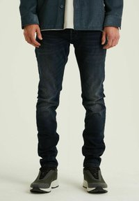 Donkerblauwe slim-fit jeans met een vervaagde textuur. Gepaard met grijze sneakers met een opvallende witte zool en zwarte veters.