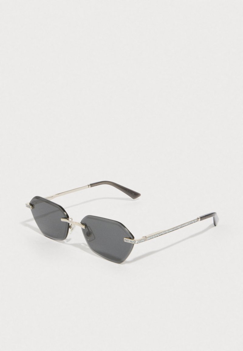 Lunettes de soleil octogonales grises avec une monture en métal doré, des branches ornées de strass et des verres foncés.
