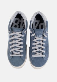 Des baskets en suède bleu clair présentent un design low-top, des lacets gris et une semelle en caoutchouc blanc. L'intérieur arbore un motif noir avec une marque.