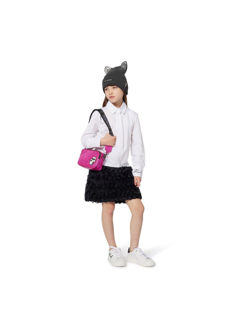 Gonna di raso nera con volant, camicia bianca con bottoni, cappello grigio a maglia con orecchie da gatto, borsa a tracolla rosa con grafiche, sneakers bianche.
