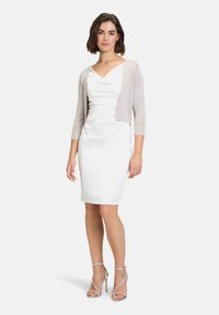 Fehér selyemruha, melynek összegyűrt bodice-ja van, rövid, világosszürke, csillogó kardigánnal párosítva. Strasszos ezüst magas sarkú szandálok tökéletesítik a megjelenést.