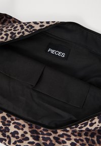 Interno di una borsa leopardata nera e marrone con chiusura a zip, foderato di nero e dotato di una tasca interna con etichetta che recita "PIECES."