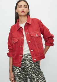 Red denim jacket with button closures, two front pockets, and white stitching. Worn over a white top and paired with leopard-print pants.