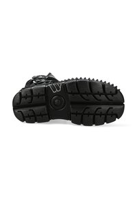 Black rubber sole with deep treads for traction, rounded shape, and circular accents. Textured surface with visible patterns for improved grip.